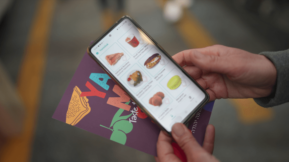 Hands holding a smartphone with Yamishuk tasting options and a colorful card